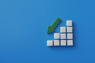 Sugar reduction concept with sugar cubes and a green arrow on a blue surface