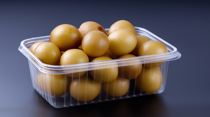 A clear plastic container holds several light-colored longan fruits with a green leaf, set against a blue background.
