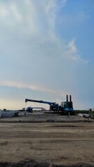 A construction site with heavy equipment used for installing building pillars, surrounded by stacked materials and open land under a wide, blue evening sky.