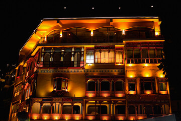 Ornate multi-story building with intricate wooden balconies and arched windows, illuminated warmly...
