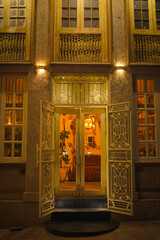 An ornate doorway opens into a warmly lit interior, revealing vintage decor, indoor plants, and a...