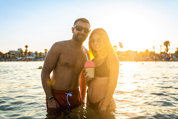 Happy couple enjoying sunset at the beach with refreshing drink