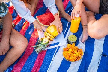 Friends enjoying picnic with pineapple, watermelon, nachos, and juice