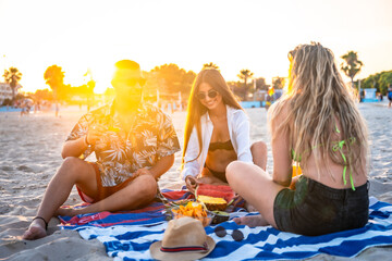 Friends eating watermelon and pineapple at sunset on beach towel