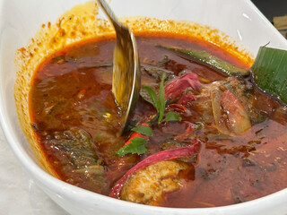 Red snapper in spicy, sourm tangy broth, garnished with herbs and chili, a bold traditional Malaysian dish known as Asam Pedas Ikan Merah.
