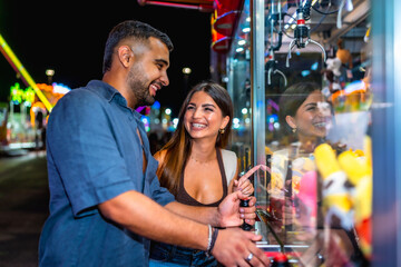 Obraz premium Happy couple playing claw crane game at amusement park at night