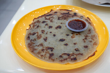 Lempeng pisang served on a yellow plate with sambal, a traditional Malaysian banana pancake grilled to golden perfection.