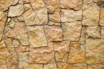 A close-up of a natural stone wall showcases its unique texture and pattern. Various shades of...