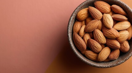 A bowl filled with raw almonds on a textured surface. The almonds are light brown with a smooth exterior. The background features a soft, muted color.