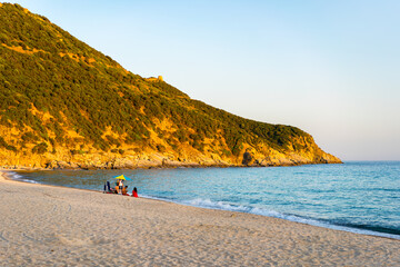 Tourists relaxing on Solanas beach at sunset in Sardinia, Italy