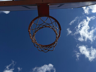 Low Angle View of Outdoor Basketball Hoop with Net against Blue Sky and Clouds on a Sunny Day
