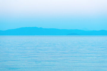 Minimalist view of calm sea with distant blue mountains under soft gradient sky. Peaceful seascape and tranquil nature concept.