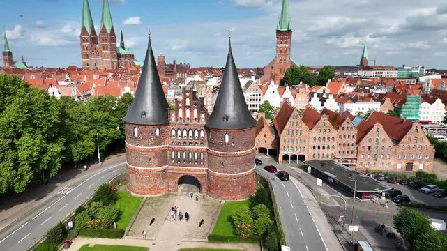 Aerial orbit of the Holsten Gate in L&uuml;beck, featuring tourists, the historic old town, red rooftops, churches and the river Trave in Germany.