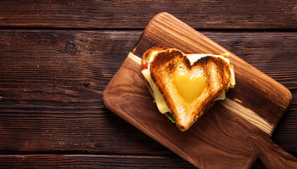 Delicious heart shaped grilled cheese sandwich, wooden cutting board. Top view tasty snack appetizer