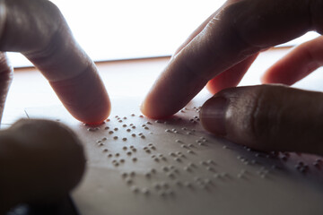 Visually impaired individuals utilize their fingertips to perceive Braille on paper, enabling them to read. Text on the paper is a dummy Lorem ipsum text.
