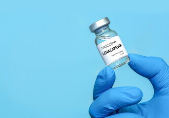 Doctor wearing blue gloves holding a vial of Lenacapavir vaccine with copy space, symbolizing...