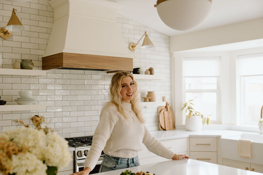 Smiling woman leaning on island in white tile kitchen