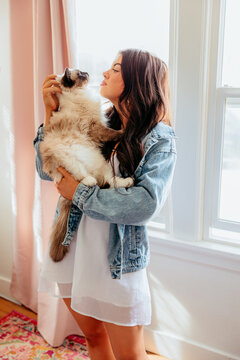 Young woman holding her fluffy cat near a window