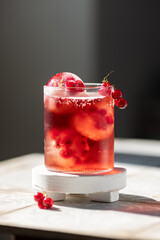 Berry lemonade in a glass with ice spheres with frozen red currant berries