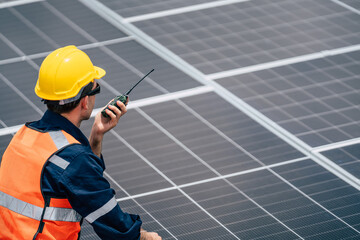 Worker communicates while installing solar panels on a rooftop during a sunny day in an urban...