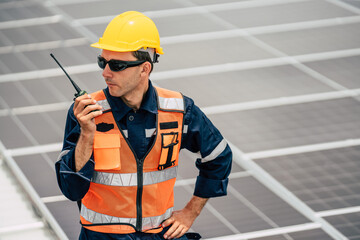 Worker inspects solar panels on rooftop while communicating via radio in bright sunlight