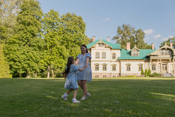 Obraz premium A happy woman and her daughter running through the grass in nature, with a wooden house in the background