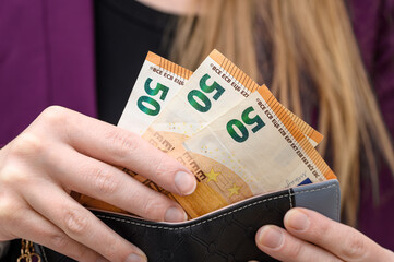 A woman paying cash in a shop, taking euro banknotes out of her wallet