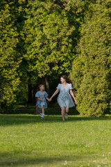 On a beautiful summer day, a mother and daughter are playing and running around the park.