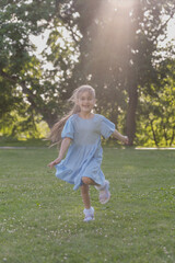 On a warm summer day, a little girl in a blue dress runs happily across the lawn in the sunlight.
