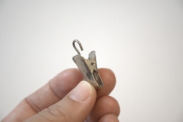 Single metal curtain clip held in a hand on white background with copy space, home textile accessory for hanging