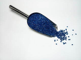 Blue plastic masterbatch, polymer carries colorful pigments with small scoops poured into a white...