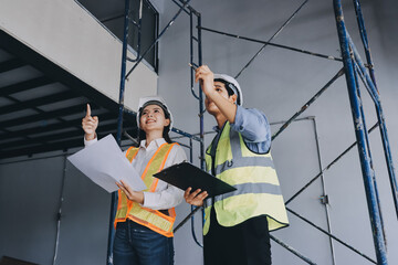 Construction manager and engineer dressed in orange work vests and hard helmets explore...
