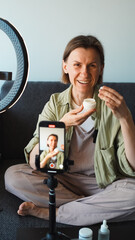The blogger opens and shows a bottle of cosmetics to her phone's camera, which is mounted on a...