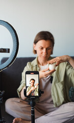 The blogger opens and shows a bottle of cosmetics to her phone's camera, which is mounted on a...
