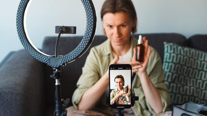A blogger shows a bottle of cosmetics to her phone camera, which is mounted on a tripod and...