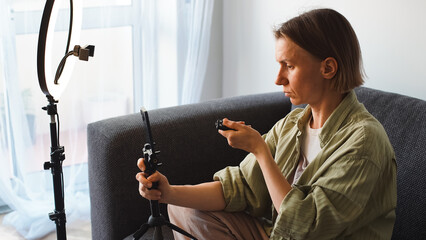 A blogger is sitting on the couch at home and setting up her phone and tripod for shooting....