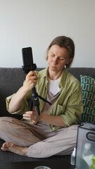 A blogger is sitting on the couch at home and setting up her phone and tripod for shooting....
