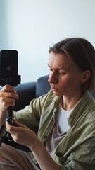 A blogger is sitting on the couch at home and setting up her phone and tripod for shooting....