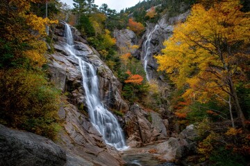 A beautiful waterfall cascades down rocky cliffs surrounded by vibrant autumn foliage in a serene forest setting