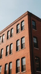 Fototapeta premium Corner of a Red Brick Building with Symmetrical Windows Against a Clear Sky