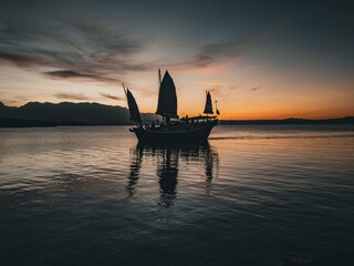 Silhouetted sailing boat at sunset on a calm sea.