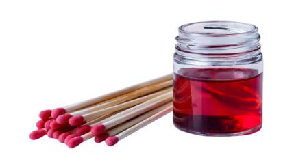A close up of matches with red tips and a glass jar filled with a red liquid on a black background