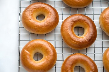 Freshly baked golden brown bagels cooling on a wire rack, showcasing soft texture and shiny crust, homemade bakery style, minimalist food photography on white background.
