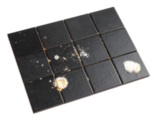 A rectangular black tiled surface with scattered white and beige powder residues on several tiles.
