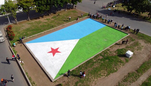 Aerial perspective of a massive Djibouti flag being unfurled on the grass by a community, a symbol of patriotism and national unity.