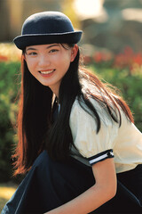Smiling young woman in a hat surrounded by greenery.