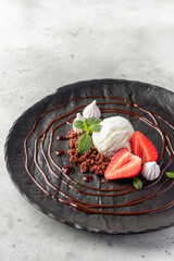 Dessert whith scoop of ice cream, strawberries, biscuit crumbs, chocolate and berry sauses on black...