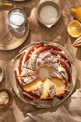 Lemon bundt cake sliced on a plate with lemon sugar glaze drips in bright morning light on beige backgrond