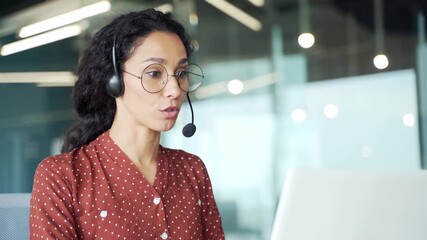 Young female corporate operator in headset working in customer support service on helpline telesale talking using laptop sitting in business office. Agent of call center advises client. Close up - Powered by Adobe
