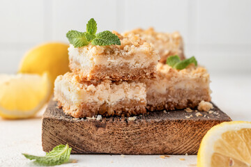 Lemon crumble bars on wooden cutting board on white tile background. Oatmeal lemon bars